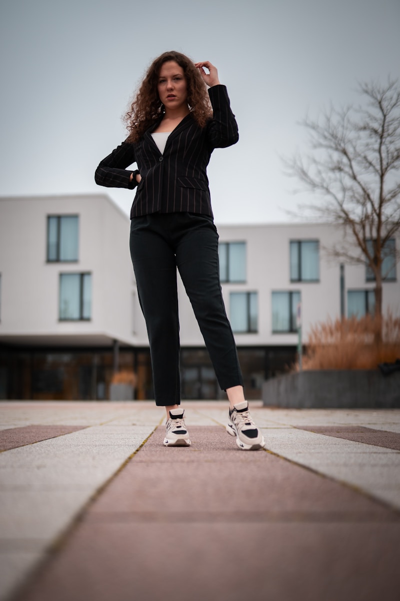 woman in black pants and white sneakers standing on gray concrete pavement during daytime